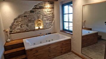 Un baño con pared de piedra, una bañera grande, escalones de madera y una ventana con detalles azules.