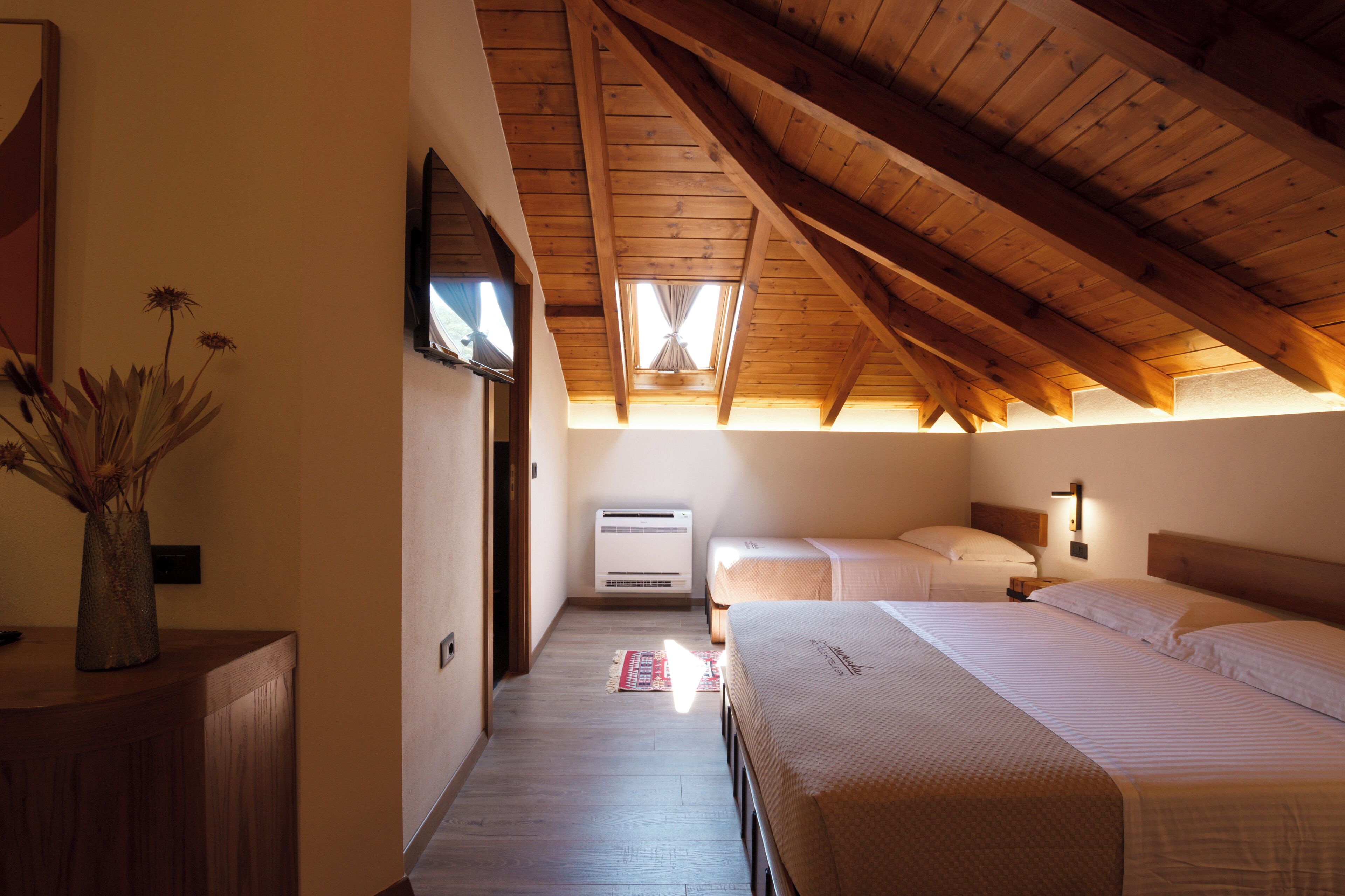 A room with a sloped wooden ceiling, a bed, a bedside table, and a wall-mounted air conditioner.