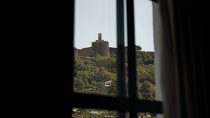 A view through a window of a historic building with a prominent tower, surrounded by lush greenery. - Cumaku Boutique Hotel & Spa (Gjirokastër)