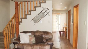Een woonkamer met een bruine leren bank, een houten trap en een eethoek op de achtergrond.
