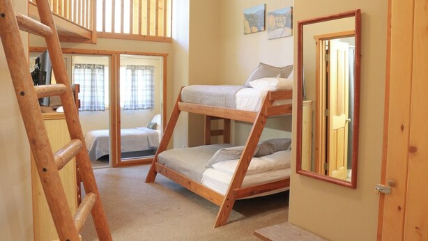 Een slaapzaal met stapelbedden, een houten ladder, een schuifdeur en een spiegel aan de muur.