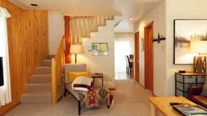 Un salon chaleureux avec un escalier, un canapé, une table basse et, au fond, un coin repas.
