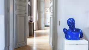 Een hal met witte deuren, een houten vloer en een blauw buste beeld op een voetstuk.