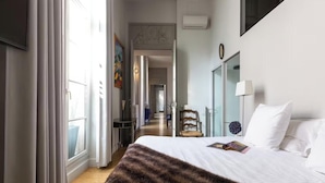Een hotelkamer met een groot bed, uitzicht op de gang en een deur naar buiten.