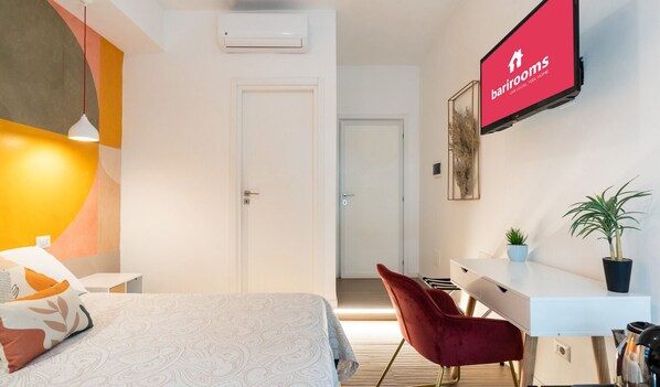A modern hotel room with a bed, a desk, a chair, and a TV displaying the barrooms sign. - Barirooms - Urban 163 (Bari)