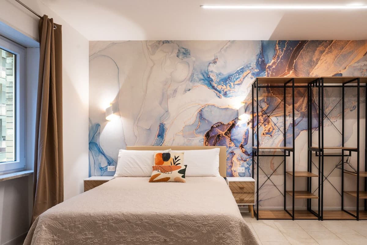 A modern bedroom with a large bed, a marble wall mural, and a built-in shelving unit.