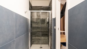 A modern bathroom with a glass shower enclosure, marble walls, and a wooden vanity. - Barirooms - Urban 163 (Bari)