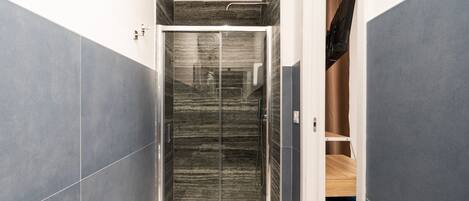 A modern bathroom with a glass shower enclosure, marble walls, and a wooden vanity.