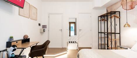 A hotel room with a bed, a desk, a chair, a wardrobe, and a TV displaying the barrooms logo.