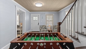 Una habitación con una mesa de fútbol, una escalera y dos sillones junto a una ventana.