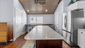 Una cocina con una isla grande, armarios de madera, un refrigerador de acero inoxidable y una ventana con persianas.