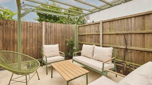 A covered patio with a wooden table and two chairs, a sofa, and a hanging light fixture. - Host & Stay | The Beach House (Overstrand)