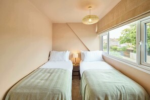 Een kleine hotelkamer met twee eenpersoonsbedden, een bedlampje, een raam met uitzicht en een hanglamp.