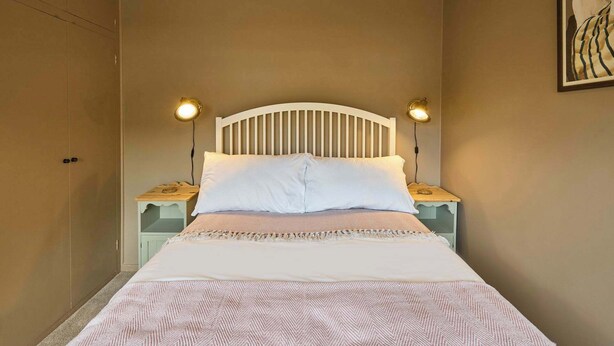 A bedroom with a bed, two bedside lamps, a nightstand, and a wall-mounted picture. - Host & Stay | The Beach House (Overstrand)