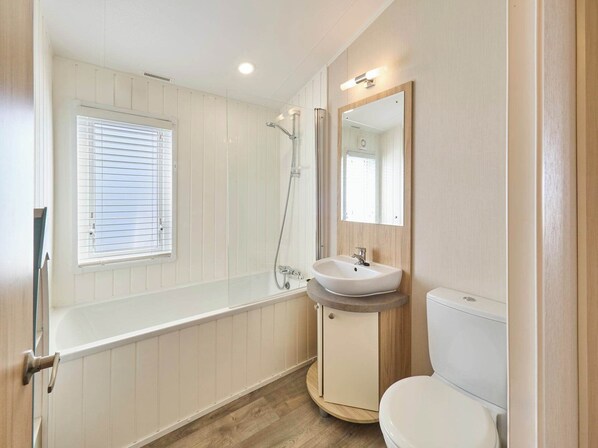 A bathroom with a bathtub, a sink, a toilet, and a window with blinds.