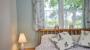 A bedroom with a wooden headboard, floral bedding, a bedside lamp, and a window with floral curtains. - Host & Stay | The Lodge (Briston)