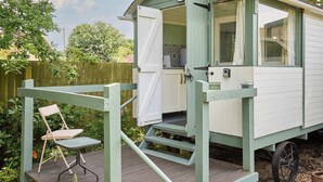 Une petite maison mobile composée d’une seule pièce, avec une porte ouverte, un petit porche doté d’une chaise et une fenêtre.