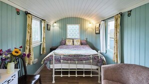 Une chambre à coucher avec un lit, une chaise, une commode et une fenêtre avec des rideaux.