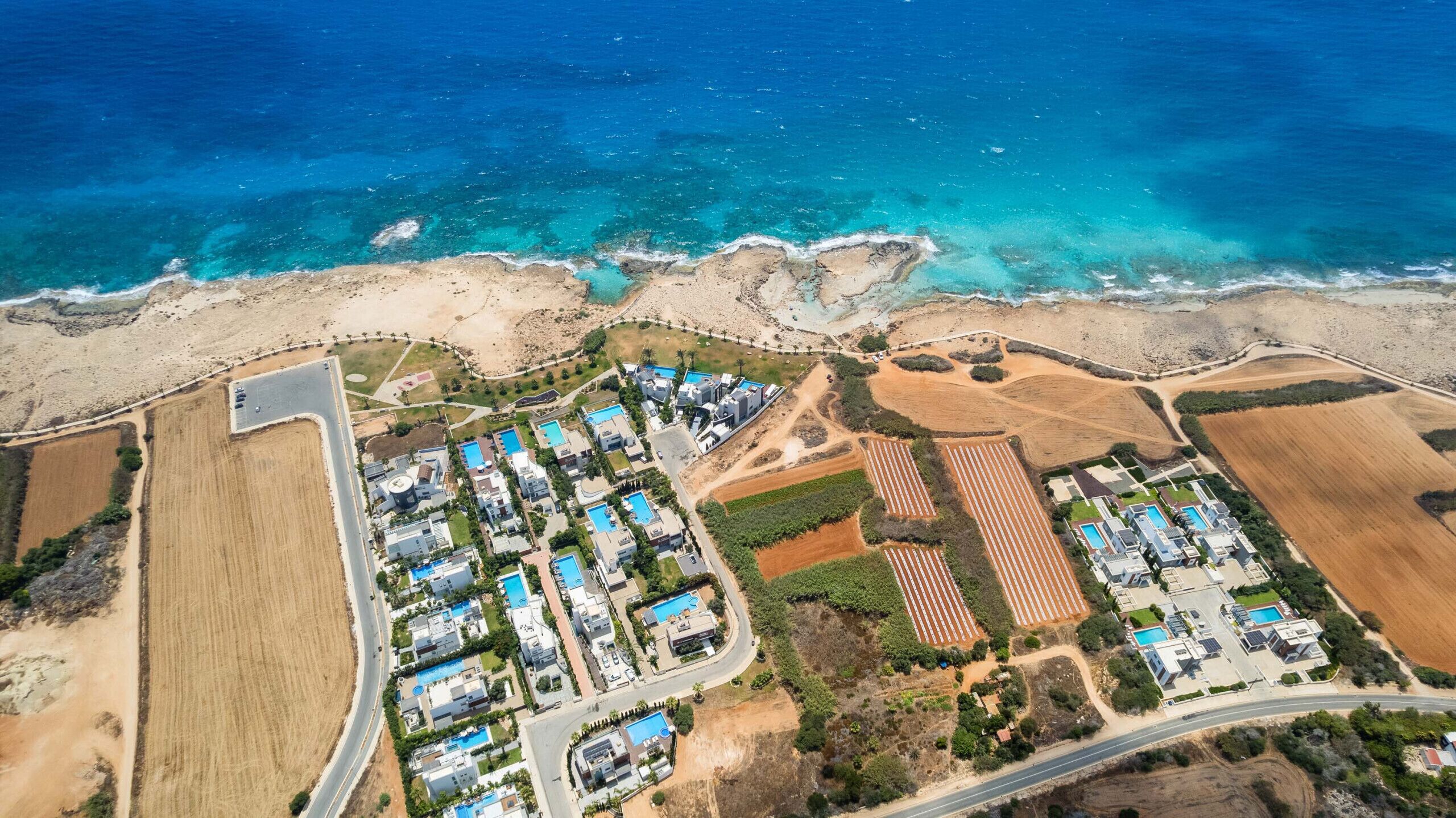 An aerial view of a coastal resort with multiple buildings, swimming pools, and a beach.