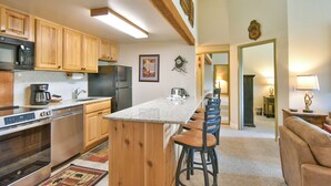 A kitchen with wooden cabinets, a built-in microwave, and a refrigerator. There is a bar area with stools and a large mirror. - Trails End Après Penthouse Condo - Ski In/Out, Walk Downtown! (Breckenridge)
