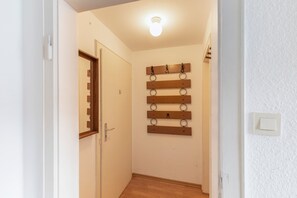 Un passadís amb una porta de fusta, un llum al sostre i una prestatgeria penjada a la paret amb objectes rodons.