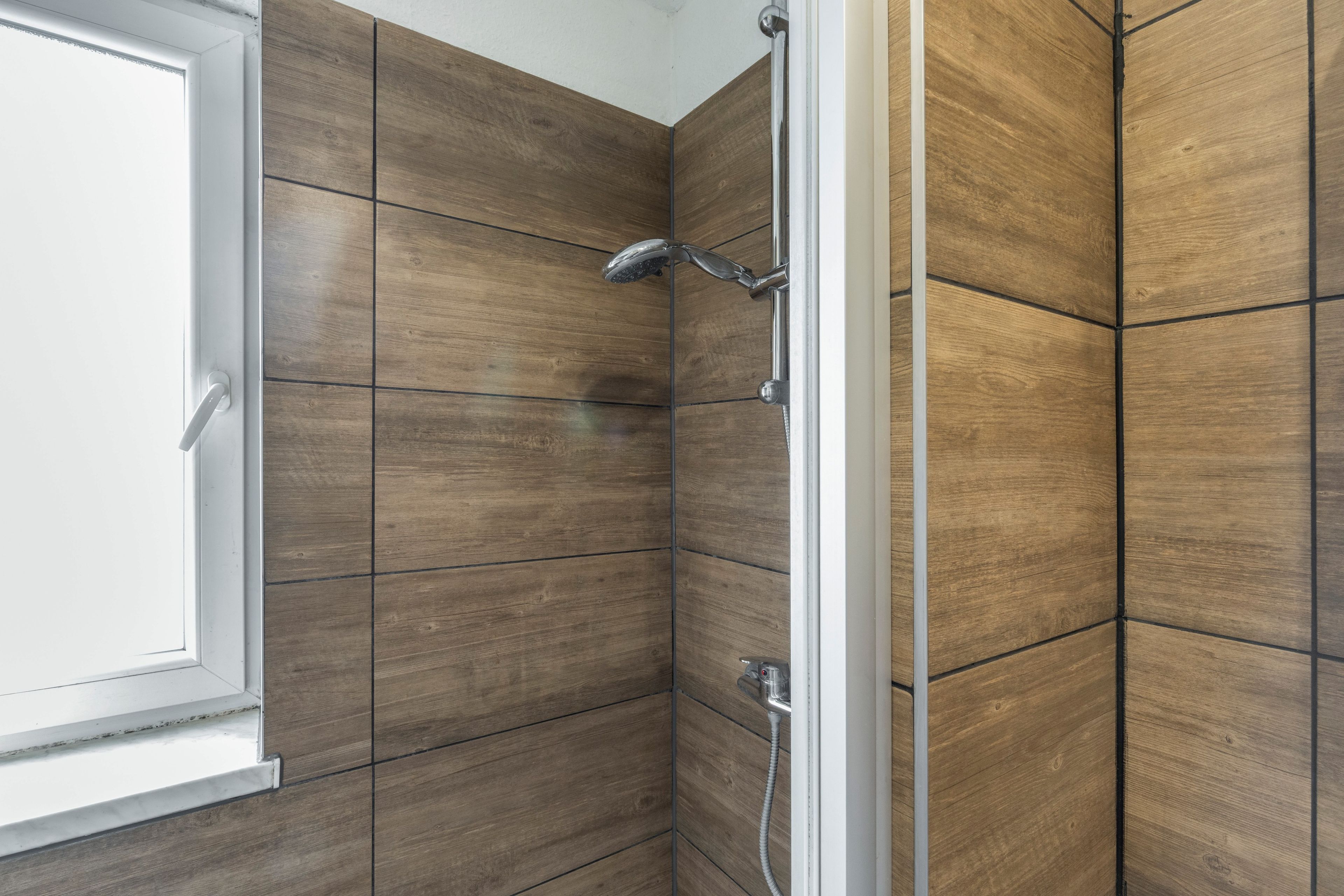 Een douche met een handdouche en een bediening op de muur.