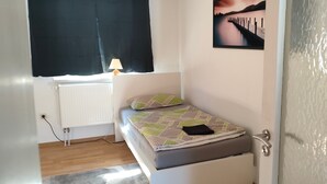 A small bedroom with a bed, a window with curtains, a radiator, and a wall-mounted picture. - Holiday Apartment 'D' in Miltenberg (Miltenberg)