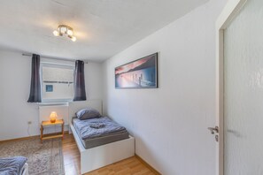 A bedroom with a bed, a bedside table with a lamp, a window with curtains, a radiator, and a painting on the wall. - Holiday Apartment 'D' in Miltenberg (Miltenberg)