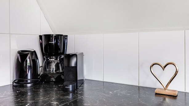 Un comptoir de cuisine avec une machine à café, une bouilloire et une cafetière. On peut y voir une décoration en forme de cœur.