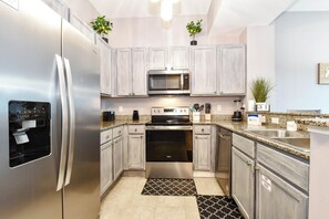 A modern kitchen with stainless steel appliances, light wood cabinets, granite countertops, and a black and white patterned rug.