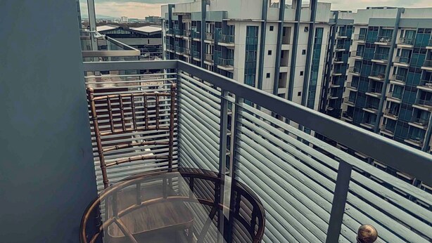 A balcony with a round glass table and bamboo chairs, overlooking a cityscape with modern buildings. - One Palm Tree Villas Condo (Pasay)