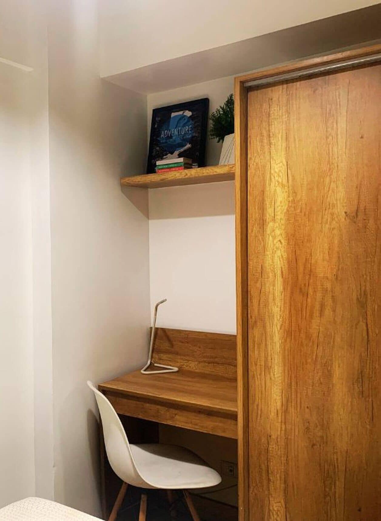 A corner room with a wooden desk, a white chair, and a bookshelf with books.