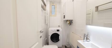 A compact bathroom with a washing machine, toilet, and sink.