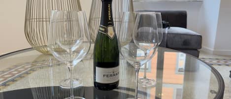 A bottle of Ferrari Brut wine on a glass table with three wine glasses.
