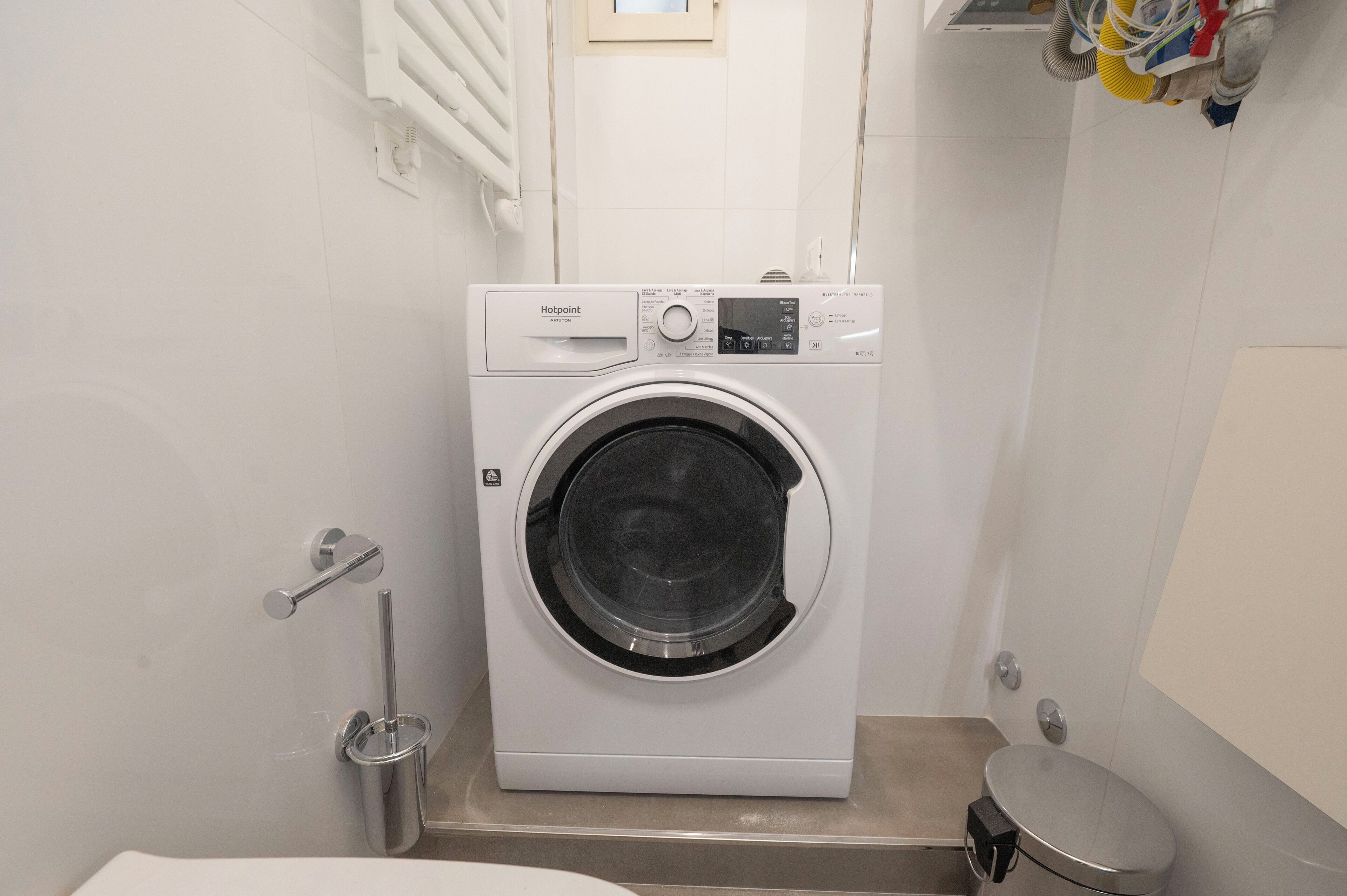 Et lille, moderne vaskerum med en frontbetjent vaskemaskine, en lille vask og et toilet.