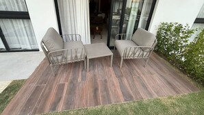 A patio with two chairs and a table, a glass door leading to an interior space, and a small green bush. - NOK Perfect 1 BR by Vistacana Rentals (Punta Cana)