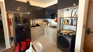 A compact kitchen with a refrigerator, stove, sink, and a washing machine. - NOK Perfect 1 BR by Vistacana Rentals (Punta Cana)