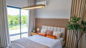 Une chambre moderne avec un grand lit, une table de chevet avec une lampe, une plante en pot et une vue sur la verdure à l’extérieur.
