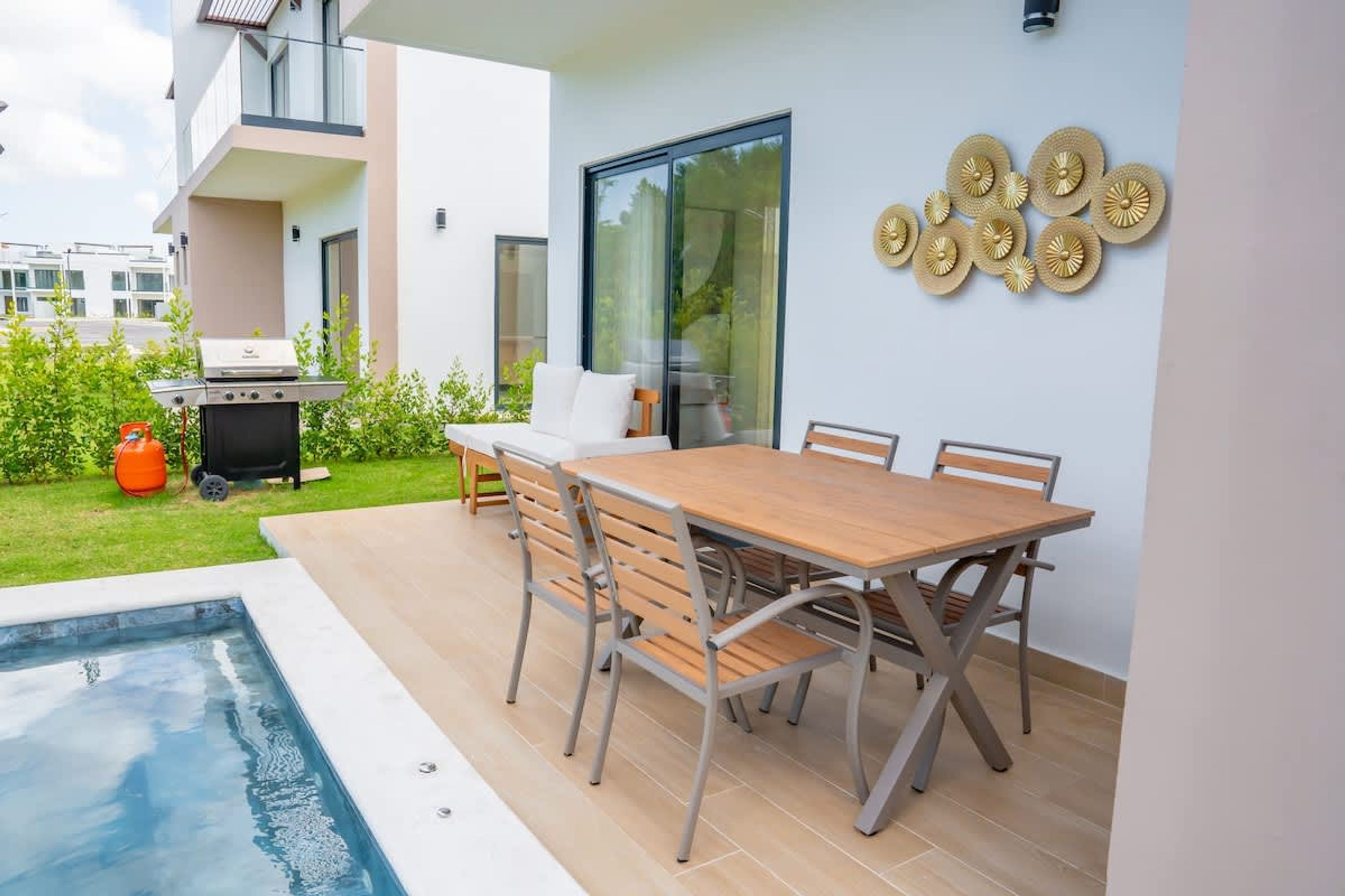 An outdoor patio with a pool, a barbecue grill, and a dining area with a table and chairs.