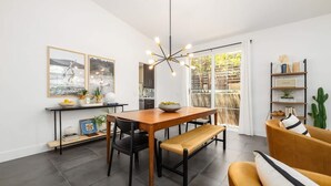 A modern kitchen with a wooden dining table, black chairs, and a bench. There is a pendant light above the table and a bookshelf with books and decorative items. - Gated Home With Pool Hot Tub (Vista)