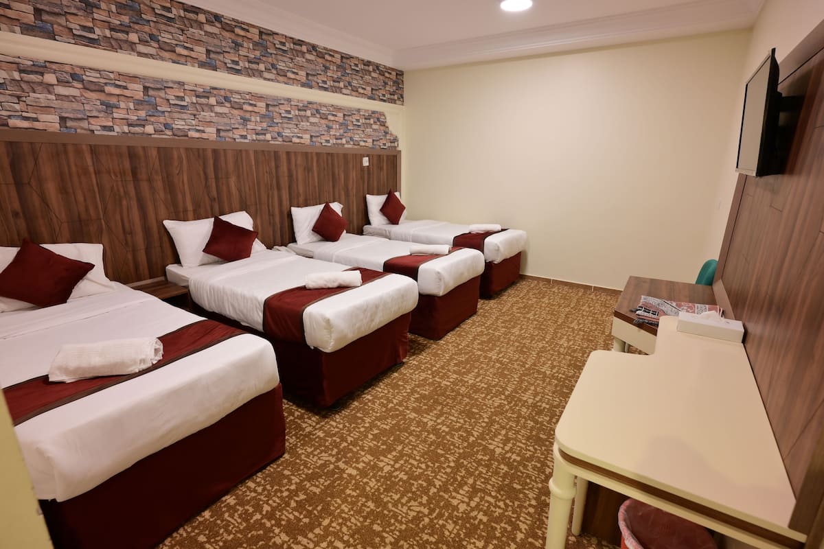 Habitación de hotel con cuatro camas, cabecera de madera, pared de acento de piedra y un pequeño escritorio con un cesto de basura.