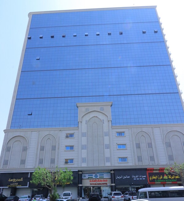 A tall building with a blue glass facade and a white lower section with arched windows and a central entrance. - Wefaq Al Saha Hotel (Makkah)