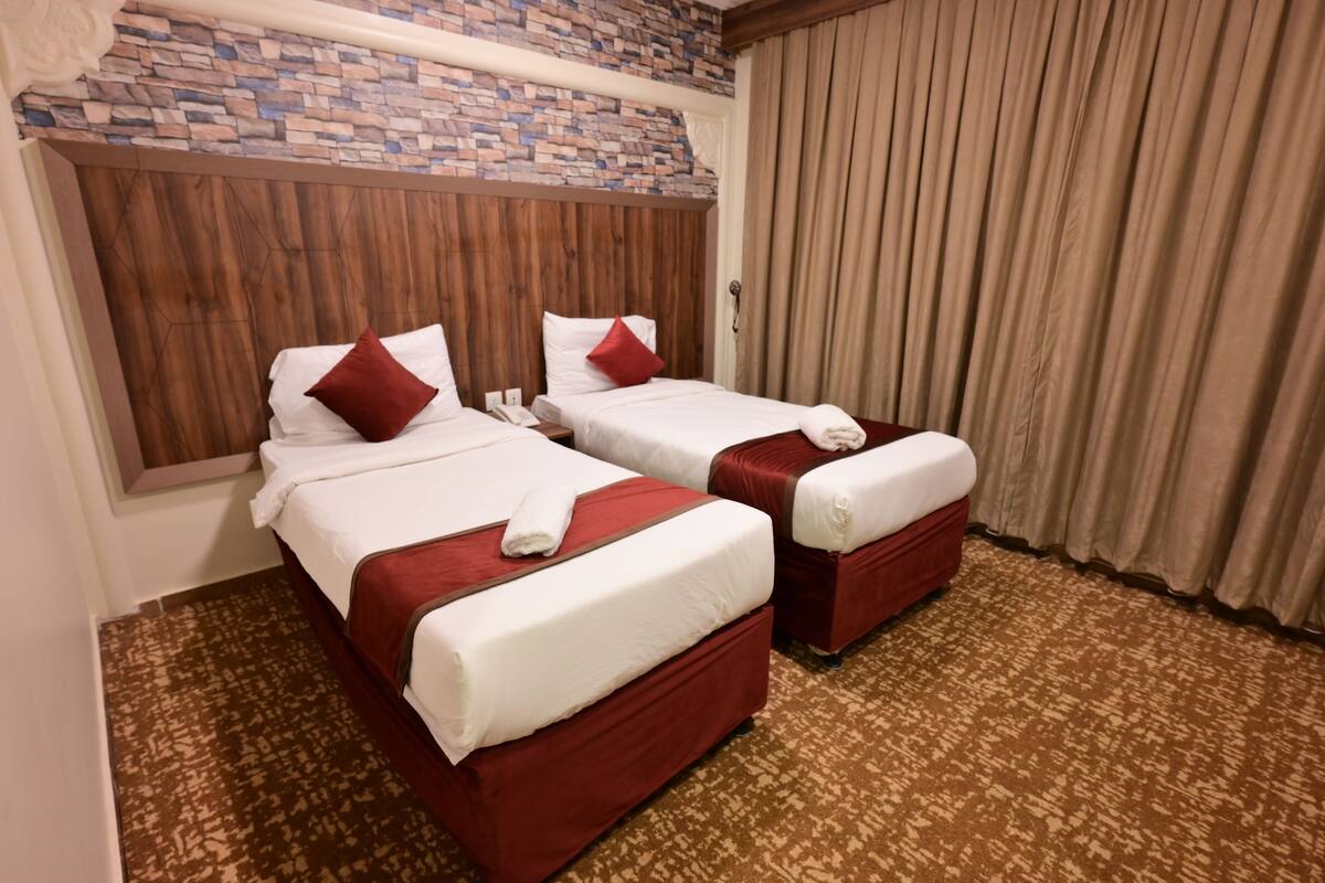Habitación de hotel con dos camas, una pared de acento de piedra, un cabecero de madera y una alfombra estampada.