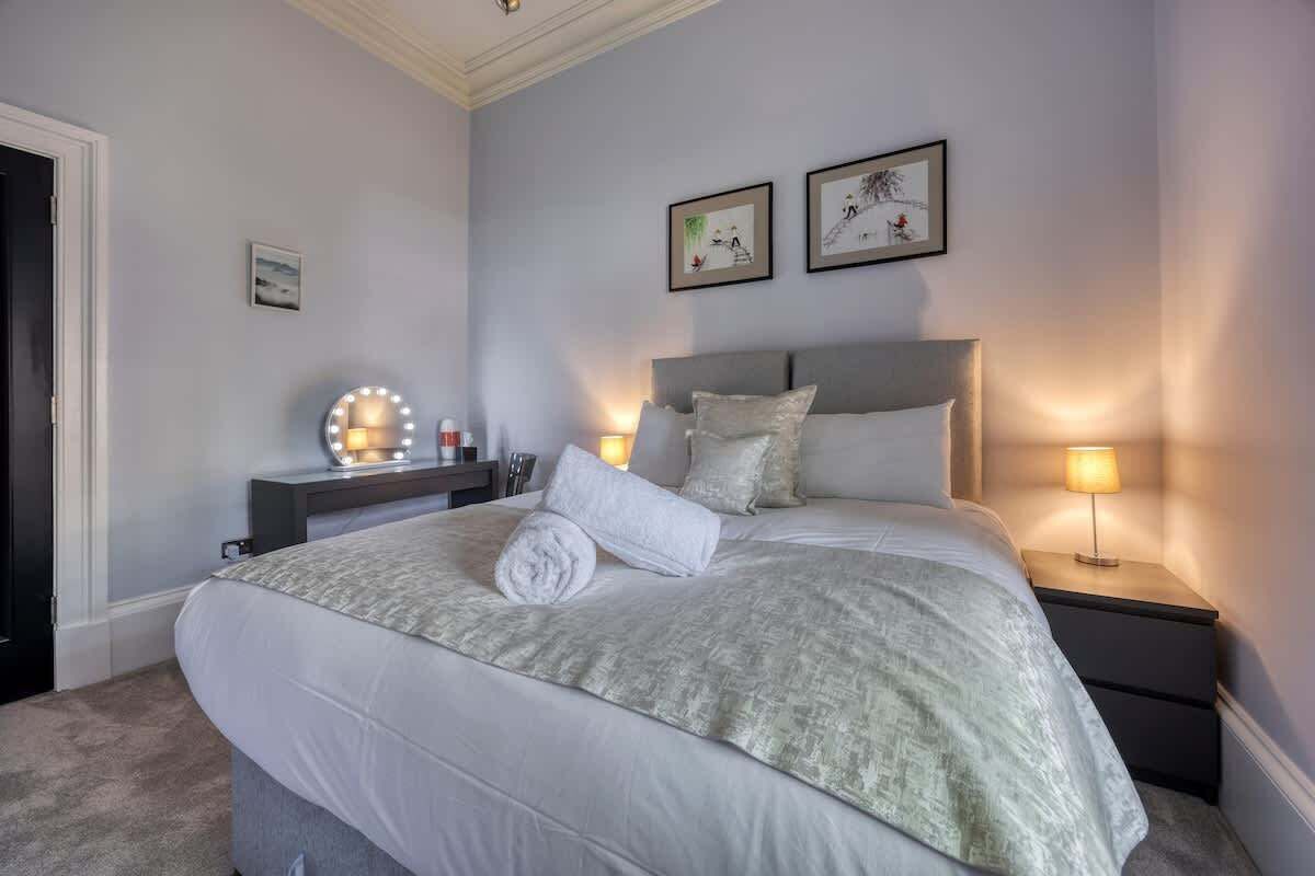 A bedroom with a large bed, bedside lamps, a vanity with a mirror, and artwork on the wall.