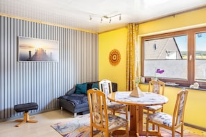 Ett rum med en randig vägg, en soffa, ett matbord med stolar och ett fönster med utsikt över ett hus.