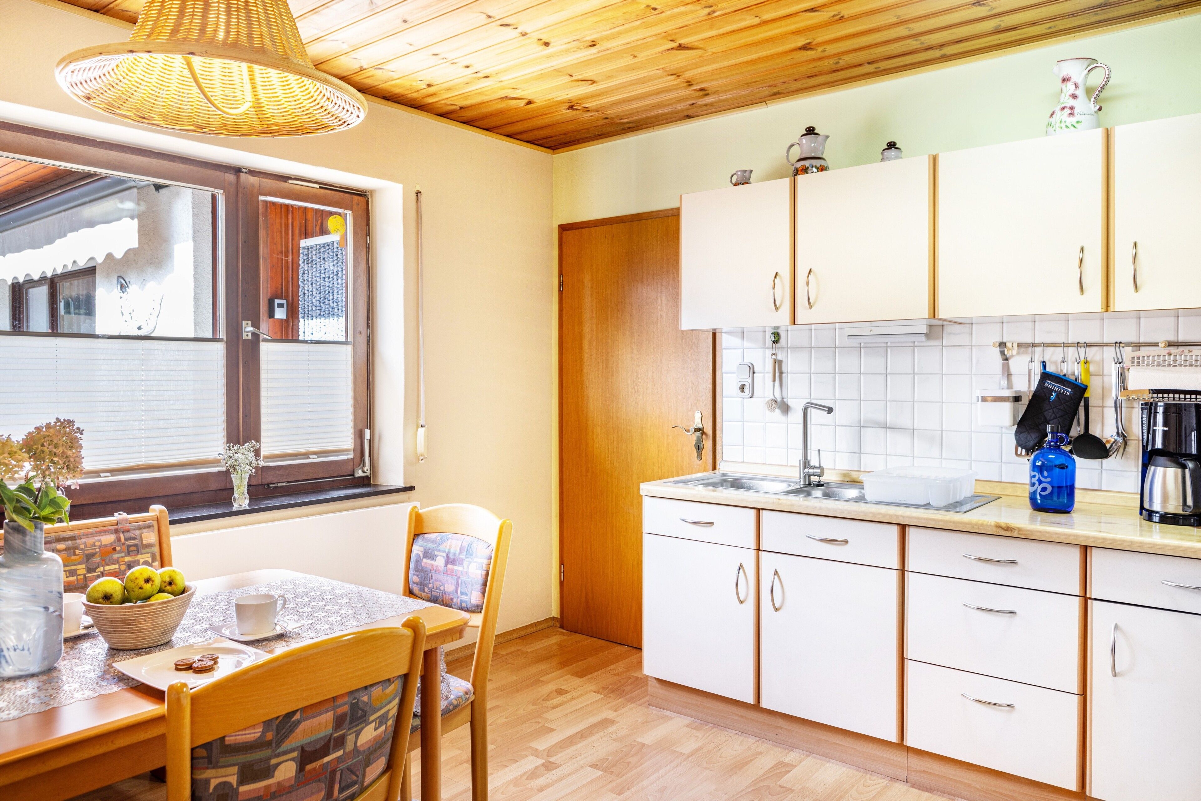 Een keuken met houten kastjes, een spoelbak en een eethoek met een tafel en stoelen.