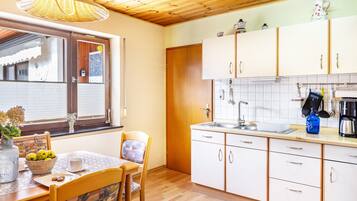 Een keuken met houten kastjes, een spoelbak en een eethoek met een tafel en stoelen.