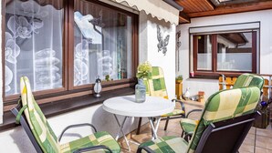 A patio with a round table, green and white checkered chairs, and a window with decorative curtains.