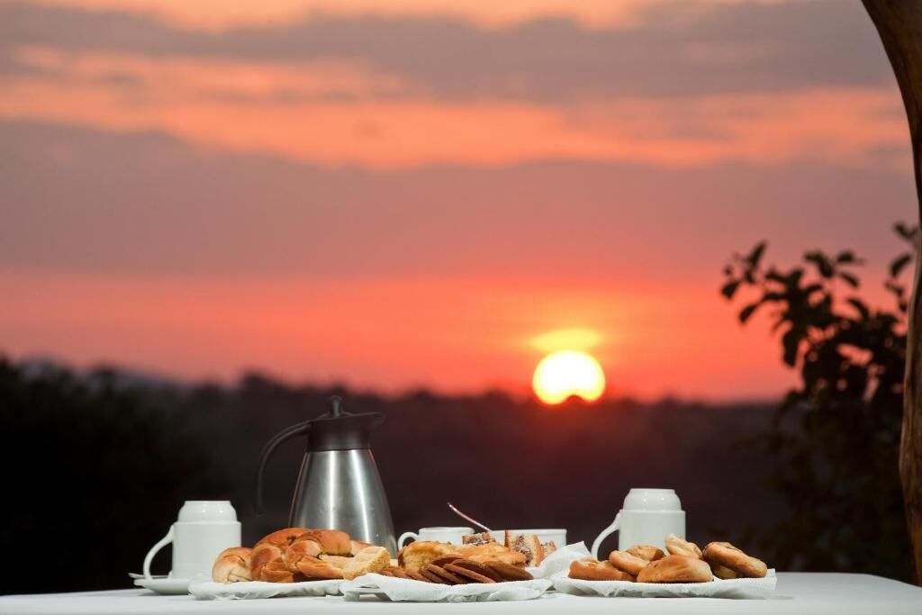 Une table avec des pâtisseries et des tasses de café, le tout mis en valeur par le décor d’un coucher de soleil.