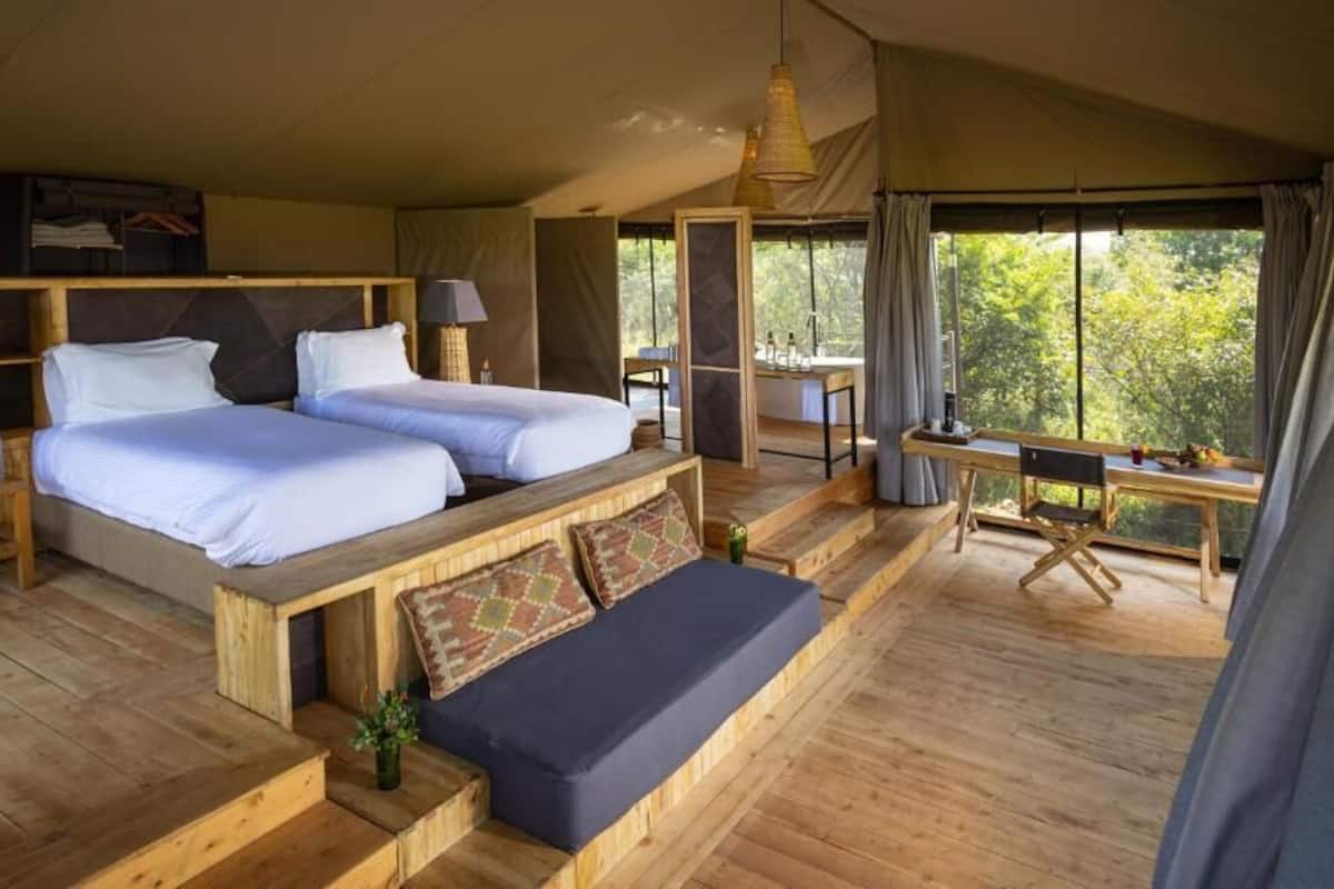 Uma cabana de madeira com duas camas, área de refeições e vista para a floresta.
